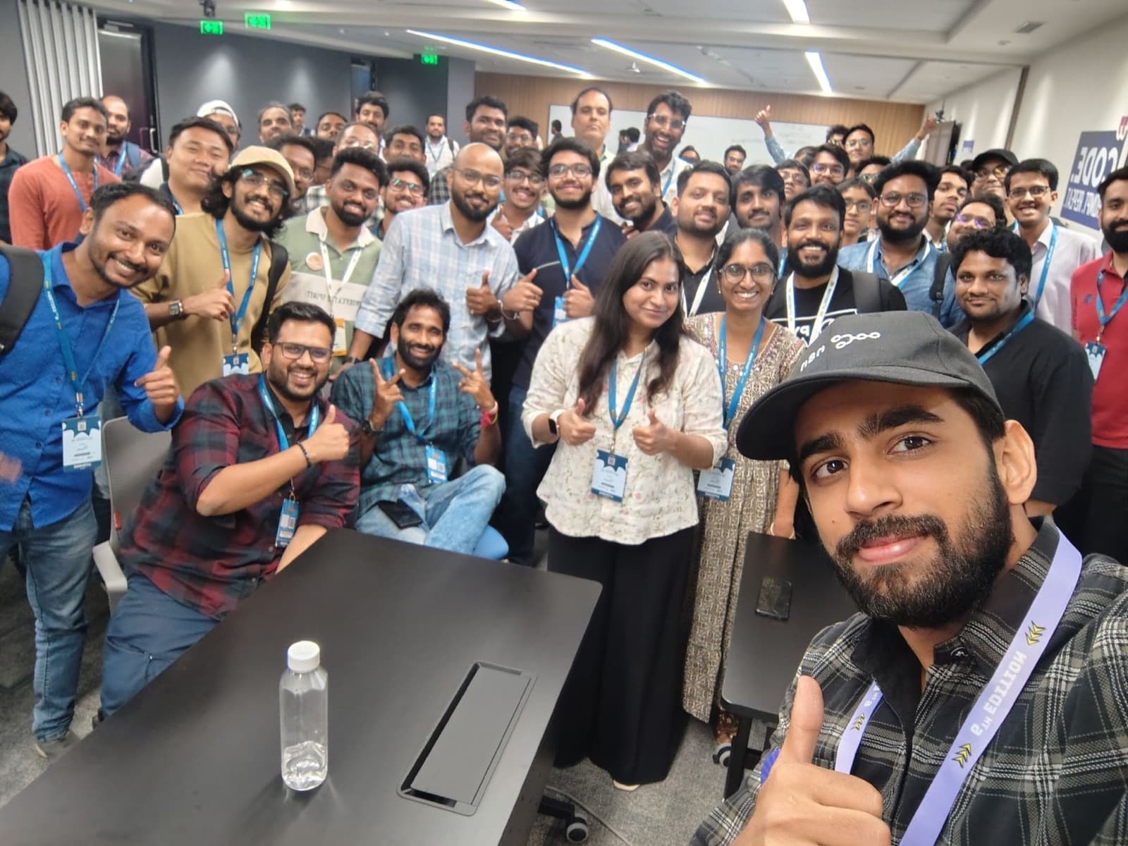 Large group of AI Anytime community members with event lanyards giving thumbs-up